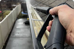 “Person holding a black pressure washer wand while cleaning a wet outdoor walkway."